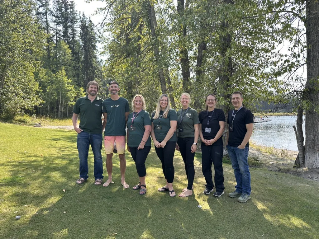 HCOS staff team standing together outdoors by a lake