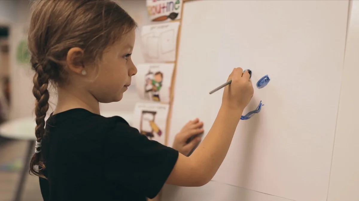 Young girl painting on a wall-mounted canvas