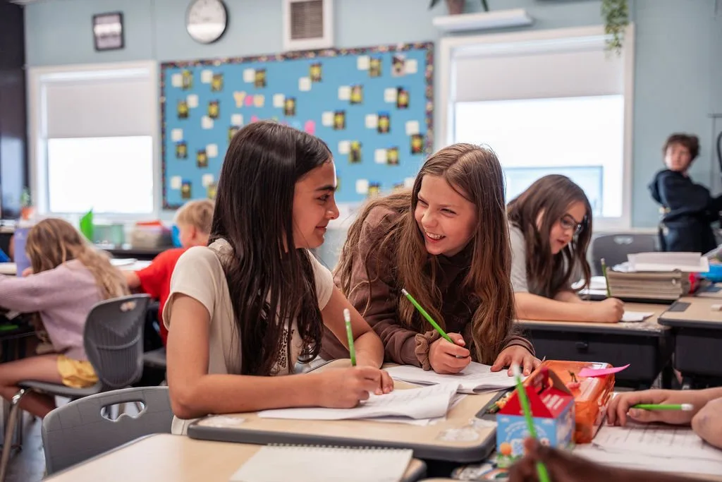 Students smiling while working together at a classroom table