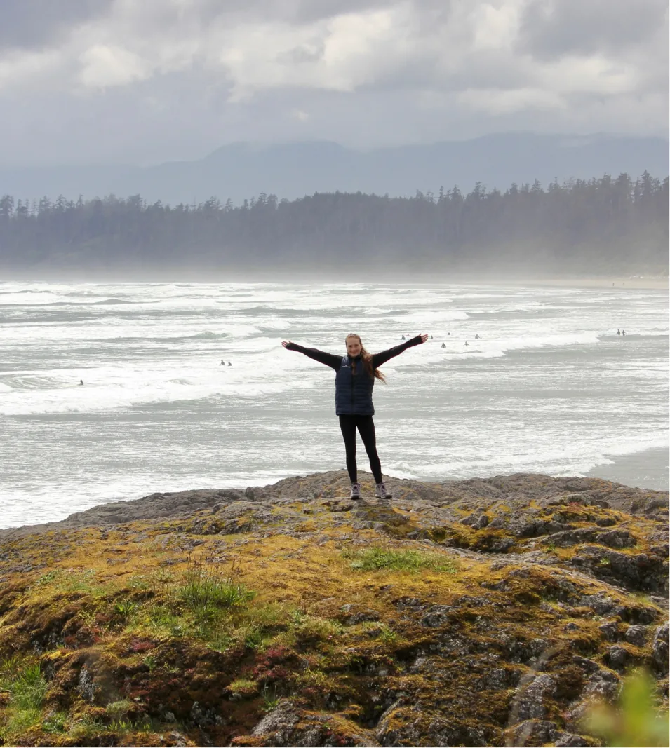 A student with arms raised on a rocky shoreline