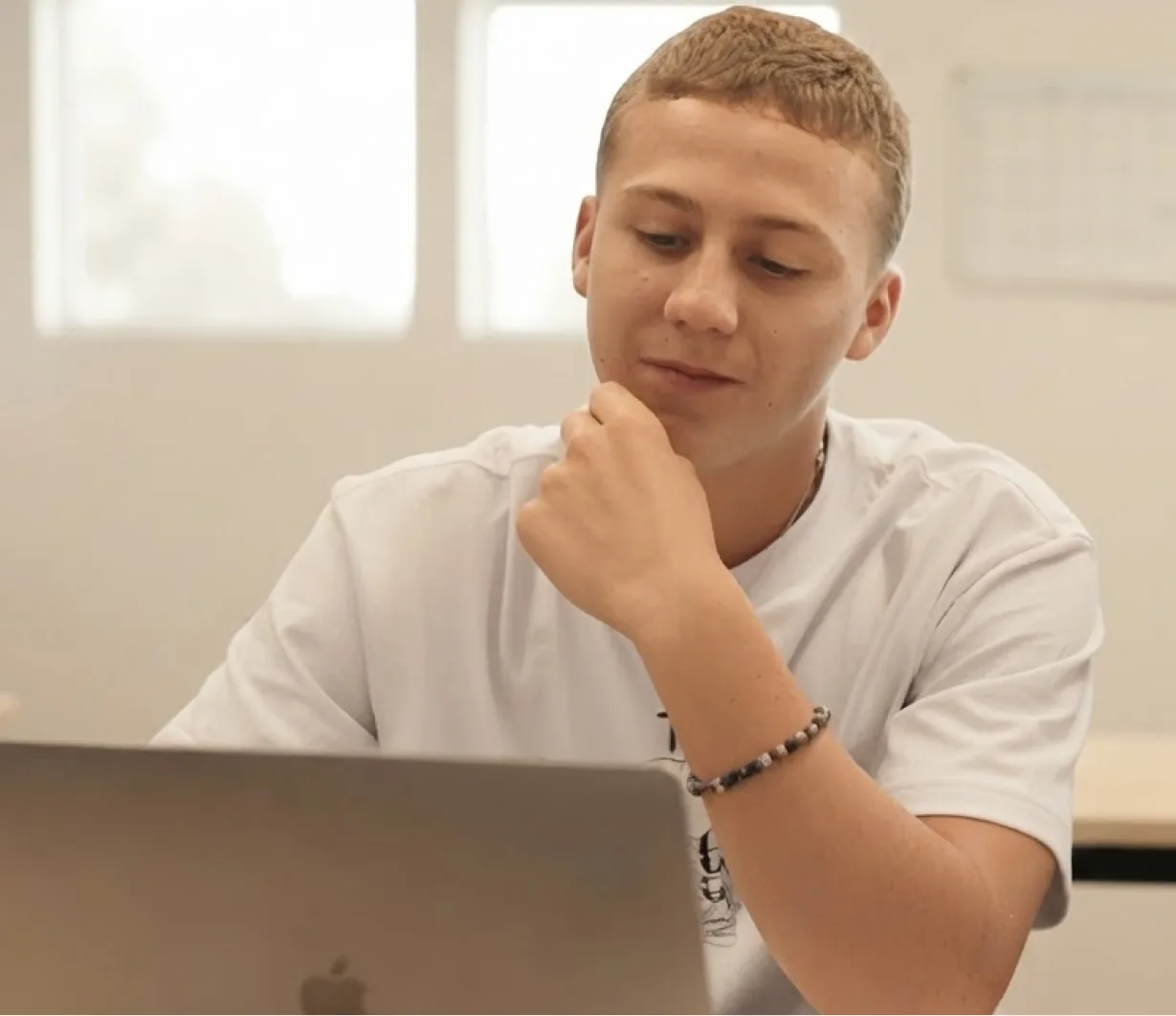 A teen student thinking while working on a laptop