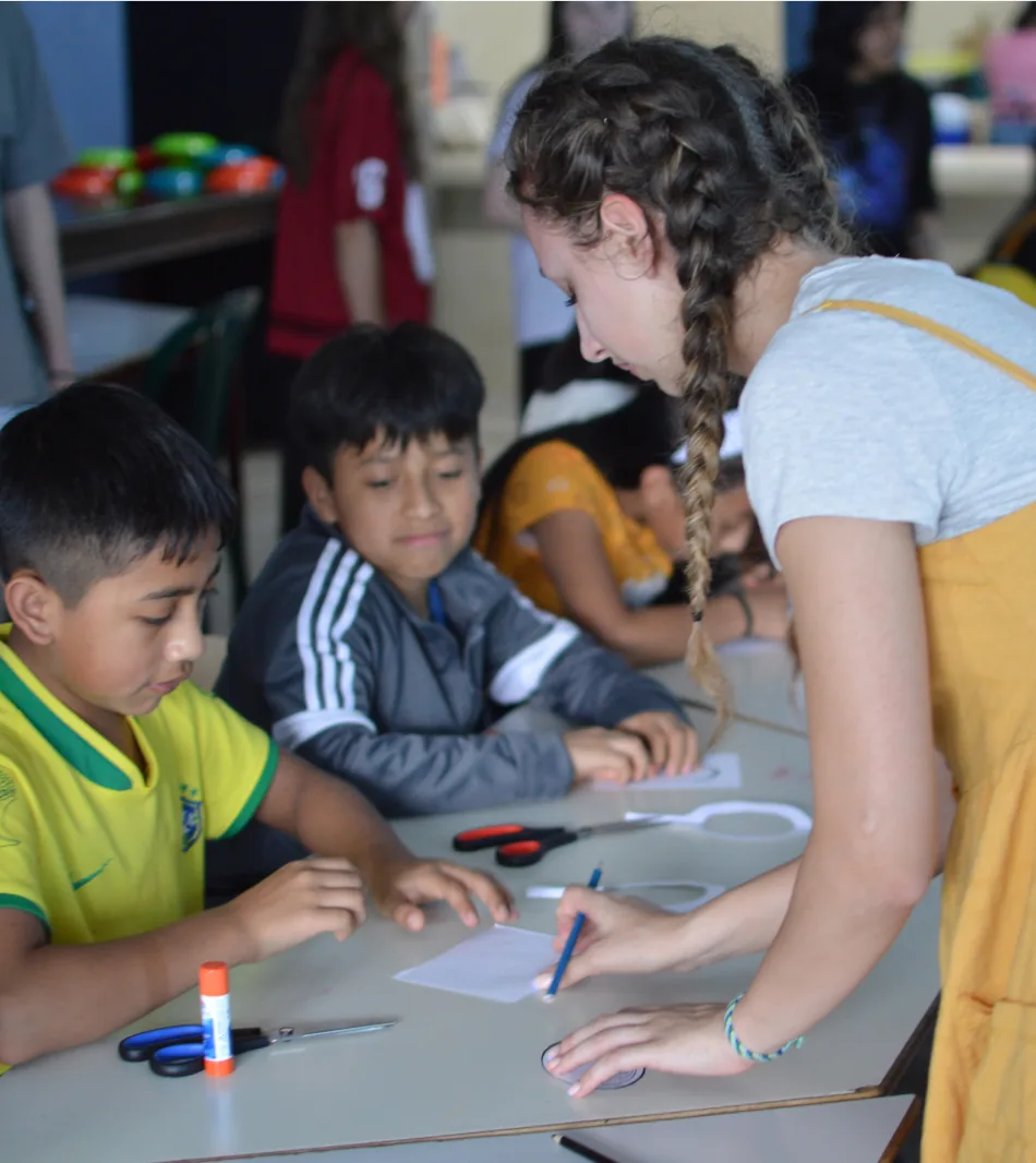 A student helping children with a craft at a classroom table