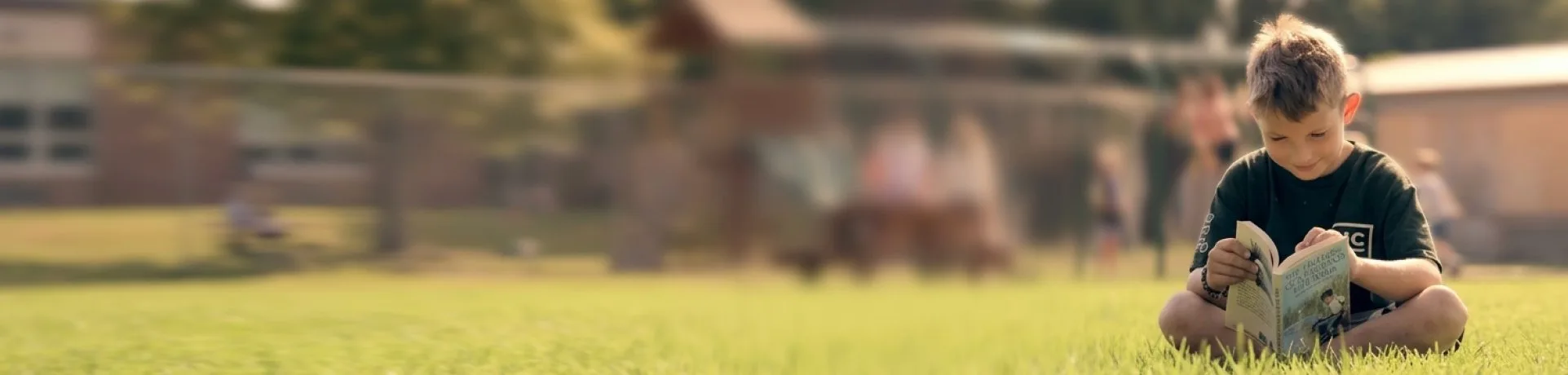 Young HCOS student reading a book while sitting in the grass